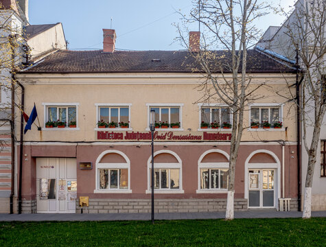 Facade of the Ovid Densusianu Hunedoara County Library in Deva, Romania, featuring traditional architecture with arched windows and flower boxes under a clear blue sky.