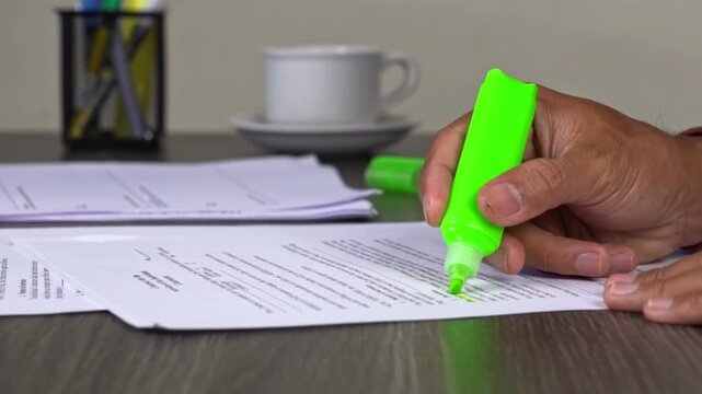 Low angle close-up of hand highlighting a business document with a green marker on a desk