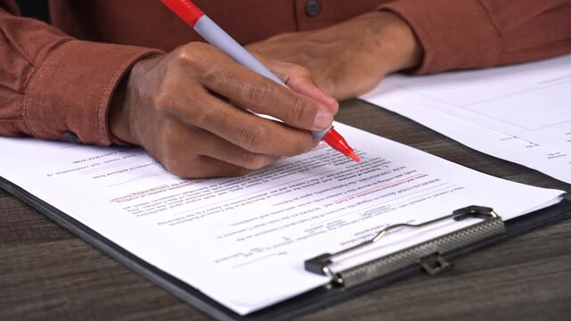 Hands highlighting key points on a business document on a clipboard with a red marker