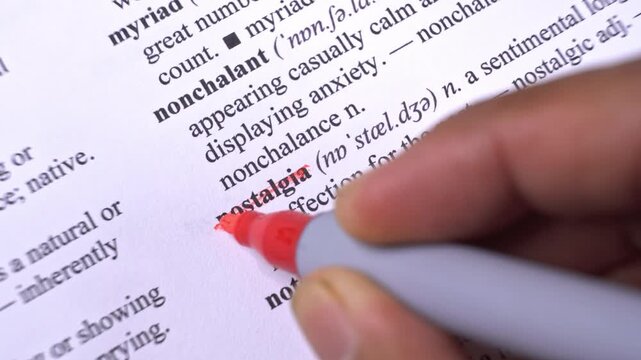 Macro close-up of a hand with a red marker highlighting text in an open dictionary
