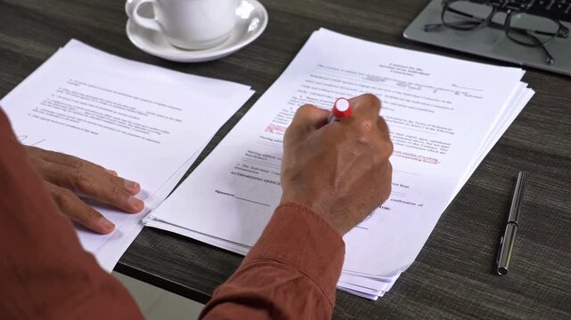 Over the shoulder view of hands reviewing a contract document with a red marker on a desk