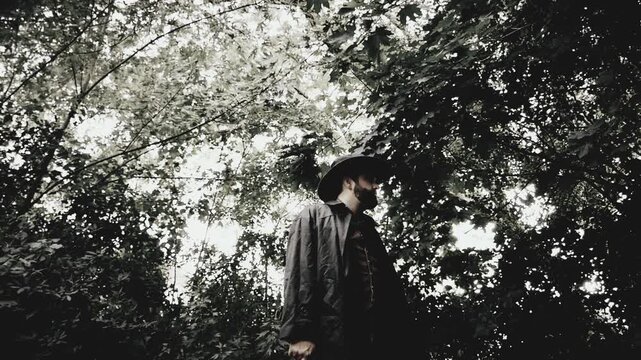 Cowboy in a duster jacket standing and holding a revolver handgun, with trees in background. Shot at a high frame rate and edited in classic vintage black and white western film style.