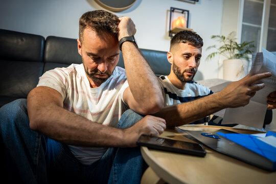 Depressed lgbt couple with heads bowed feeling defeated by financial debt.