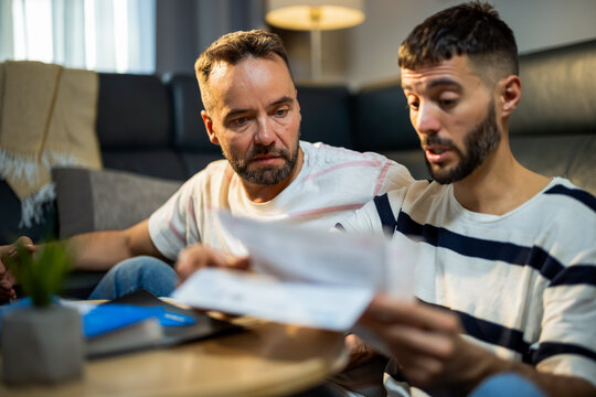Frustrated gay couple arguing and gesturing with bills in hand.