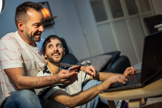 A focused same sex couple managing household finances and shopping online on a laptop.