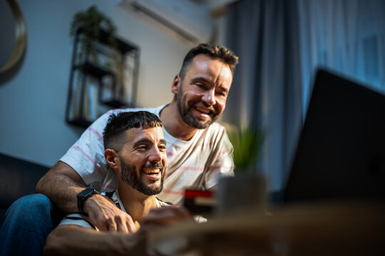 Two male partners checking their bank card details while shopping on a laptop at home.