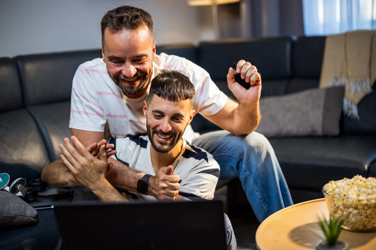 Excited same sex couple celebrating a successful online purchase with a laptop and credit card.