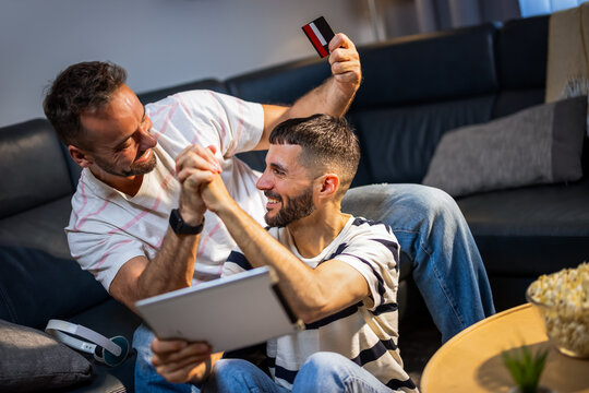 A happy same sex couple giving a high five while shopping online with a laptop and credit card.