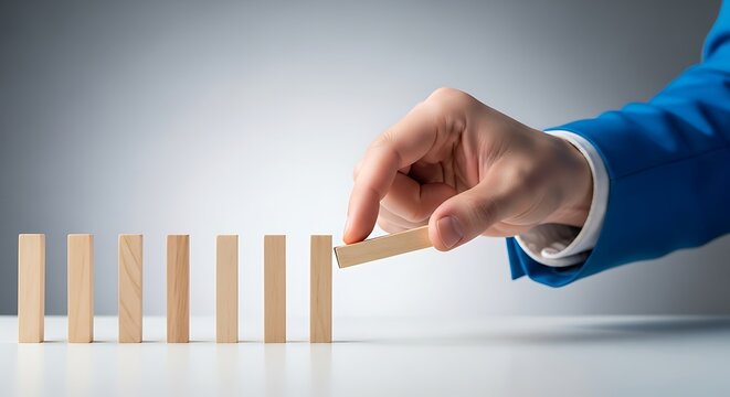 Businessman in blue suit placing final domino piece on a row of wooden blocks
