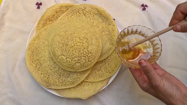 Traditional Moroccan baghrir pancakes with thousand holes, served warm with honey and butter. Semolina batter cooked on one side creates a soft texture perfect for soaking sweet syrup.