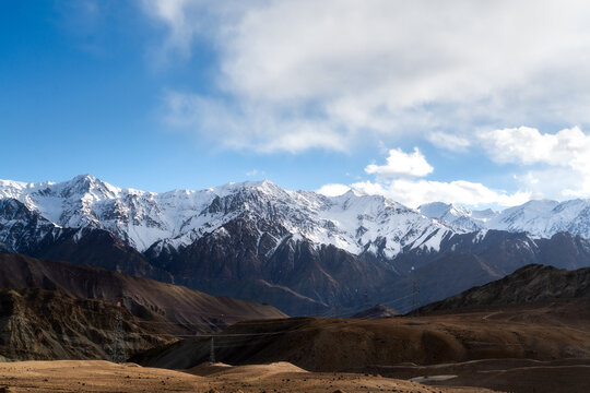 Spectacular mountain range with snow-covered peaks under a bright blue sky in Ladakh, India. High altitude desert landscape with rocky terrain and winter scenery. Panoramic view of Himalayan nature.