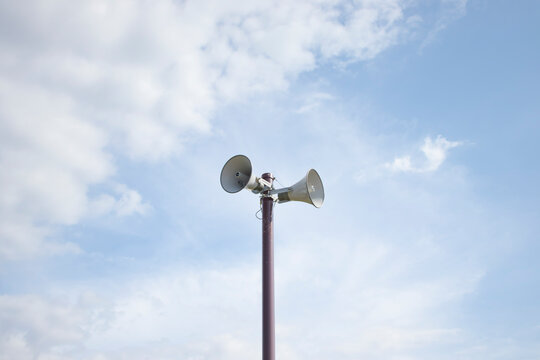 Outdoor public address speakers on pole against blue sky with clouds