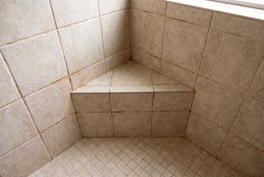 Dirty shower corner with moldy grout and beige tiles