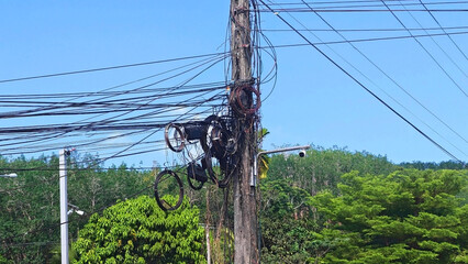 Tangled Cables on Utility Pole: A complex network of wires and cables cascades down a weathered utility pole under a bright sky, illustrating the infrastructure of modern communication © Chatchaa