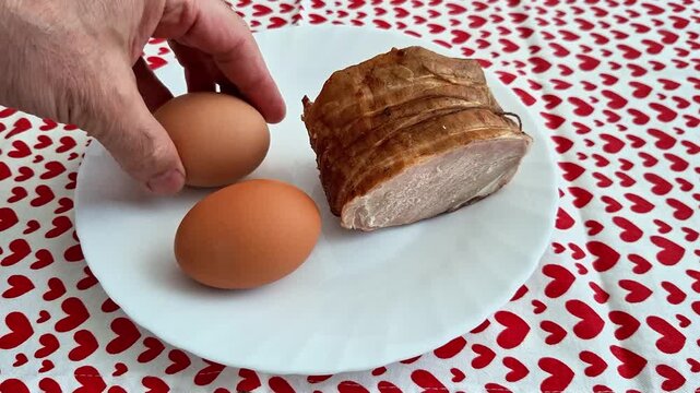 Two brown eggs and a piece of cooked meat rest on a white plate atop a red heart patterned tablecloth, highlighting a simple food arrangement with everyday dining context