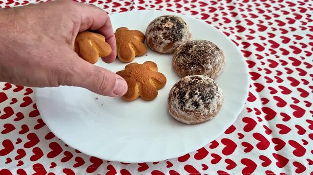 Six baked pastries, three golden flower shaped and three cocoa dusted domes, rest on a white plate atop a red heart patterned tablecloth, presenting a festive dessert arrangement