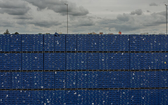 Aerial view of massive stacks of blue plastic crates in an outdoor storage yard under an overcast sky.