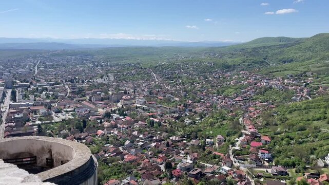 Wide-angle panoramic panning shot of Deva, Romania, taken from the historic Deva Citadel, showing the urban landscape, residential areas, and the surrounding green plai