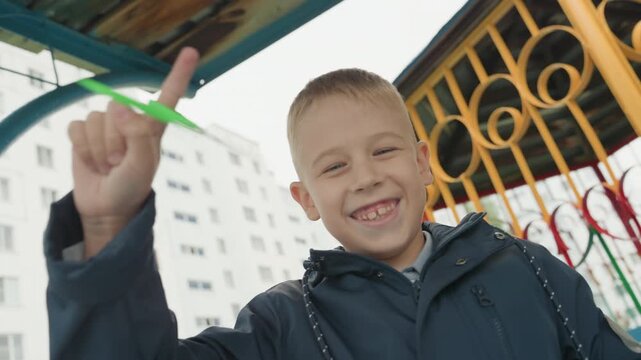 Child balances scissors with joy. Child bravely balances scissors on finger beneath playground shelter. Young boy demonstrating dexterity with scissors outdoors before beginning school day