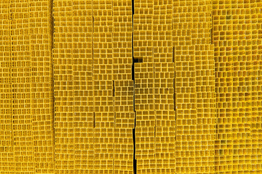 Aerial view of thousands of yellow plastic crates stacked in a dense grid pattern at an industrial site, creating a vibrant geometric texture.