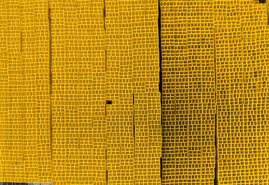 Aerial view of stacked yellow square-profile industrial tubes organized in neat vertical columns creating a repetitive geometric pattern.