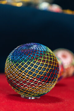 Close up of a traditional red Kaga Temari handball with intricate rainbow silk thread embroidery on display in a museum