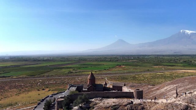 Aerial drone shot of Khor Virap Monastery near the Ararat plain in Armenia. Mount Ararat appears behind the monastery and nearby rural fields.
