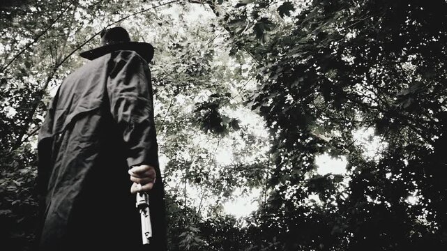 Cowboy in a duster jacket standing and holding a revolver handgun, with trees in background. Shot at a high frame rate and edited in classic vintage black and white western film style.