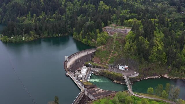 4K aerial drone footage of Lake Merwin dam and electrical substation on the Lewis River in Washington, USA. Hydroelectric power plant infrastructure surrounded by forest in Pacific Northwest landscape