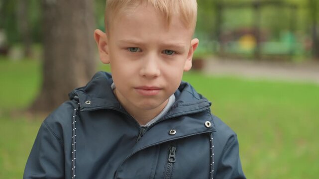 White boy on park bench preparing for back to school, close portrait frames show hesitant child tucking head into hood, thoughtful pupil meeting camera gaze, subtle smile shifting to confident
