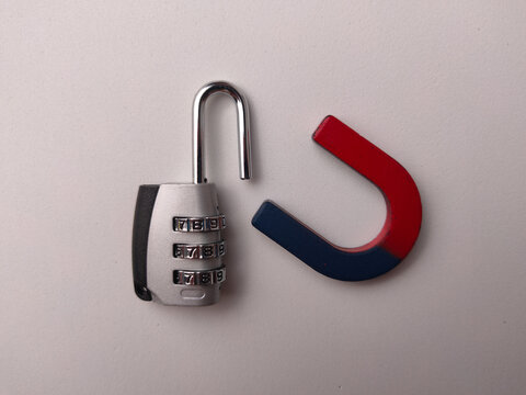 An open silver combination padlock sits next to a red and blue horseshoe magnet on a white surface