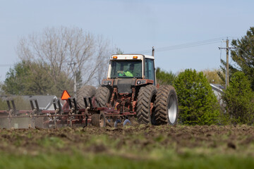 Obraz premium A farmer man in a bright green shirt driving a tractor machine on a farm field.