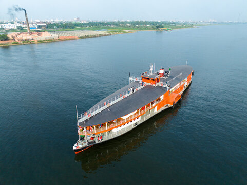 Aerial view of a large orange paddle steamer cruising on the Buriganga River near Sadarghat with people on deck and industrial buildings in the background Dhaka, Dhaka Division, Bangladesh.