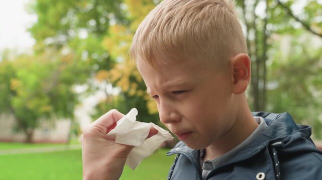White boy mom wiping face before school, outdoor park with autumn trees, tender parent action, tissue cleaning tear, nervous expression easing, morning routine preparing for school, emotional support