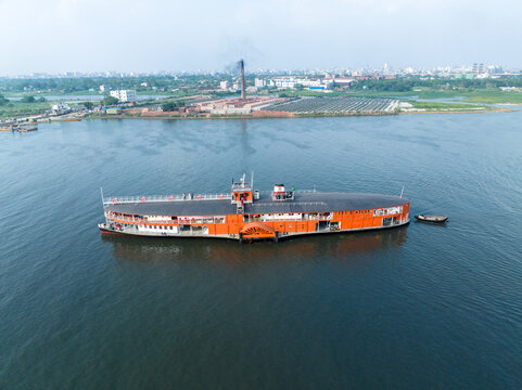 Aerial view of a large orange paddle steamer boat navigating the Buriganga River near Sadarghat with industrial chimneys in the background Dhaka, Dhaka Division, Bangladesh.