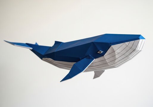 Origami whale sculpture in blue and gray paper on a plain background