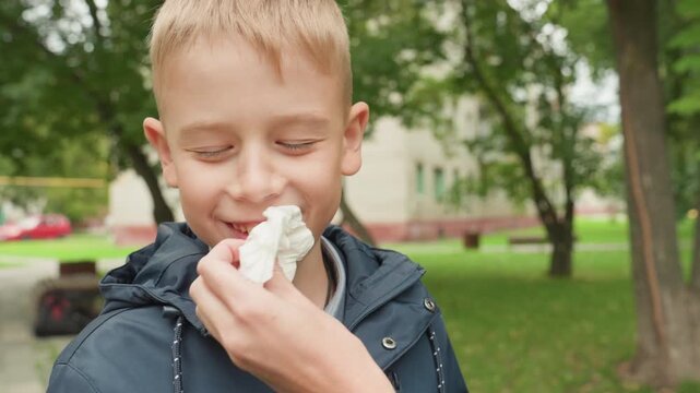 Parent wiping boy mouth with napkin, gentle school morning prep scene as parent helps student clean after snack before heading back to class, candid closeup in leafy park, supportive interaction