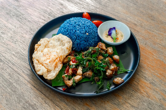 Healthy Thai pad krapow with butterfly pea blue rice salted egg dip and crispy crackers on plate
