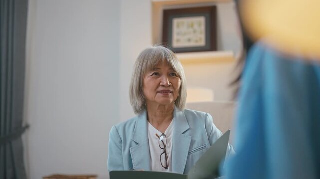 Senior Asian female psychologist taking notes during therapy session with woman patient.