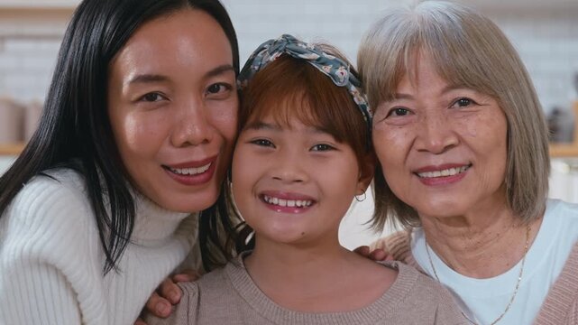 Slow motion Portrait of three generations of Asian women a cute little girl hugging her mother and grandmother while smiling and enjoying quality family time together at home bonding with love, care, 