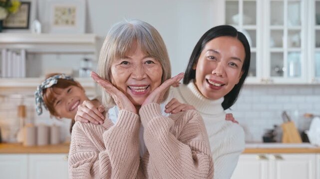 Slow motion Asian family three generations women portrait with grandmother daughter and granddaughter. The grandmother stands in front daughter and granddaughter peek out from behind.