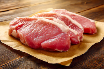 Fototapeta premium Fresh raw pork loin steaks on brown parchment paper over a rustic wooden background