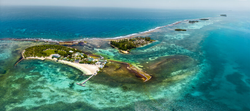 Aerial view of a tropical island with turquoise coral reefs, white sand beaches, and lush palm trees in Guanaja, Bay Islands Department, Honduras.