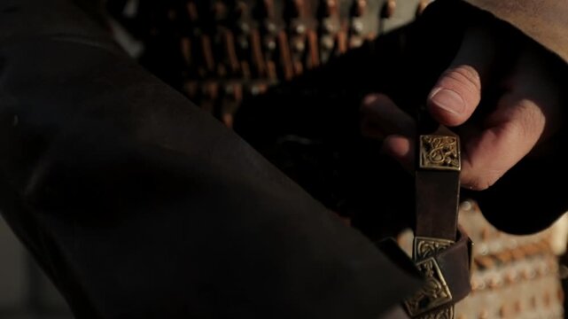 Extreme close-up of Viking warrior's gloved hands fastening leather belt on chainmail armor in dark medieval setting. Cinematic battle preparation detail shot for historical reenactment content.