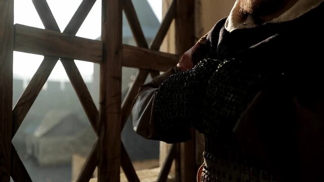 Extreme close-up of Viking warrior putting on dark iron chainmail gauntlets in sunlit wooden medieval hall. Dramatic preparation for battle scene &mdash; cinematic historical reenactment footage