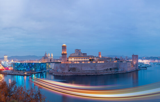 Saint Jean Castle and Cathedral de la Major and the Vieux port with motion speed light of passing ferry in the foreground at sunset - Marseille, France