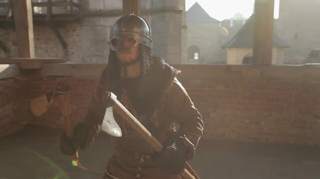 Male medieval warrior swinging battle axes in both hands inside fortress courtyard with dramatic golden backlight and cinematic lens flare. Powerful action reenactment footage for history and fantasy 
