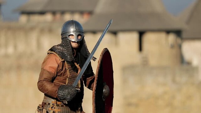 Dynamic action shot of Viking warrior in full armor thrusting sword forward with castle wall in background. Powerful combat stance cinematic historical reenactment footage for history and fantasy cont