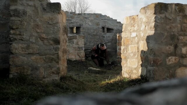 Medieval warrior moving through ancient stone ruins, crouching down and smelling the ground between weathered stone walls. Dramatic tracker cinematic scene for historical reenactment and action conten