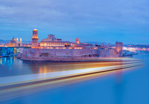 Saint Jean Castle and Cathedral de la Major and the Vieux port with motion speed light of passing ferry in the foreground at sunset - Marseille, France